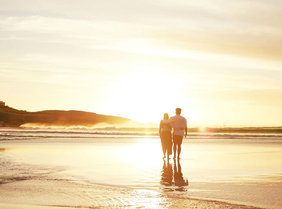 Couple walking on a beach at sunset.